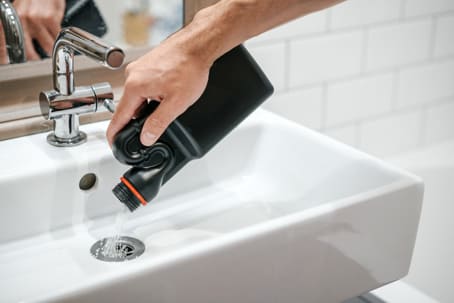 A person pours drain cleaner into a sink