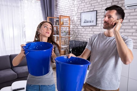 Holding a bucket catching water from a ceiling leak