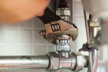 An adjustable wrench tightening a fitting on a metal pipe